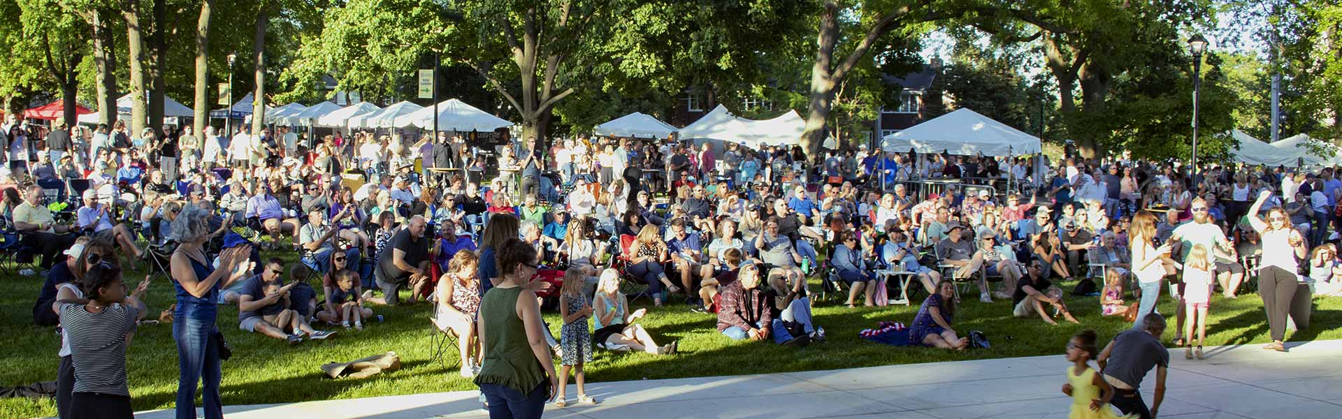 Large crowd gathered on the grass in Memorial Park for the Cream of Wheaton event, as viewed from the bandshell stage