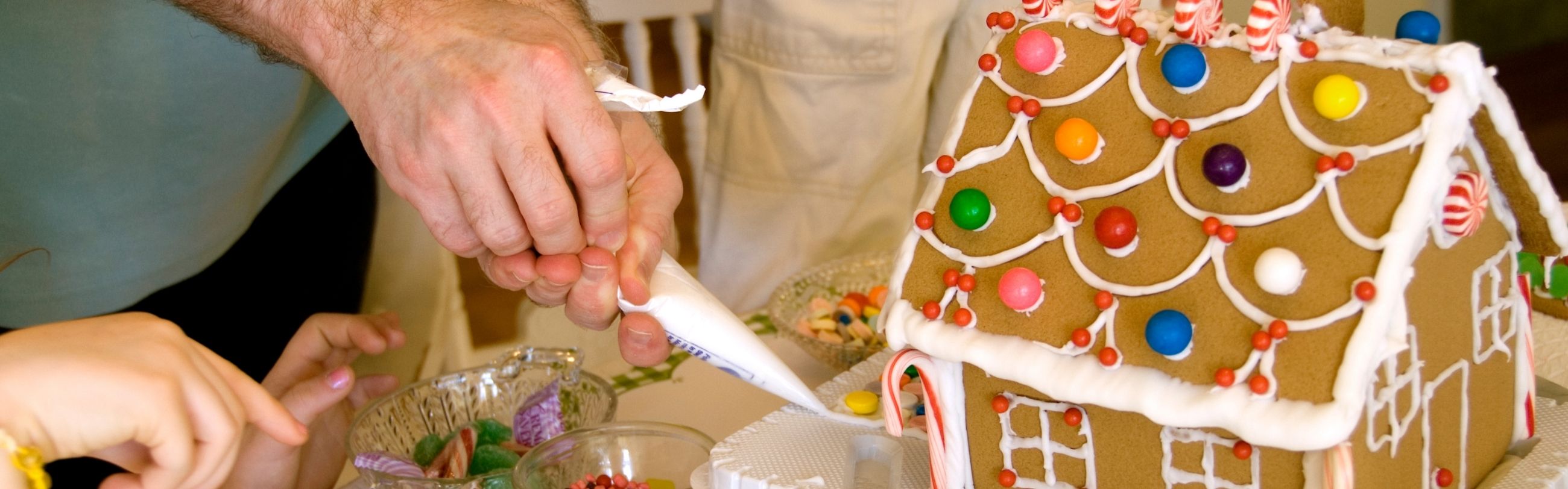 parent and child piping frosting on gingerbread house