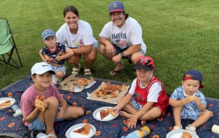 a family eating pizza on a picnic blanket on the grass