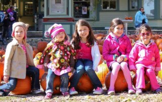 Group of little girls sitting on top of pumpkins