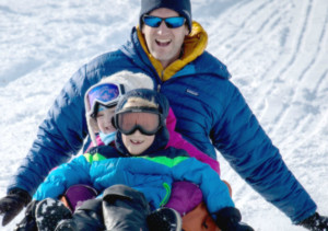 dad with his 2 kids sledding down the hill