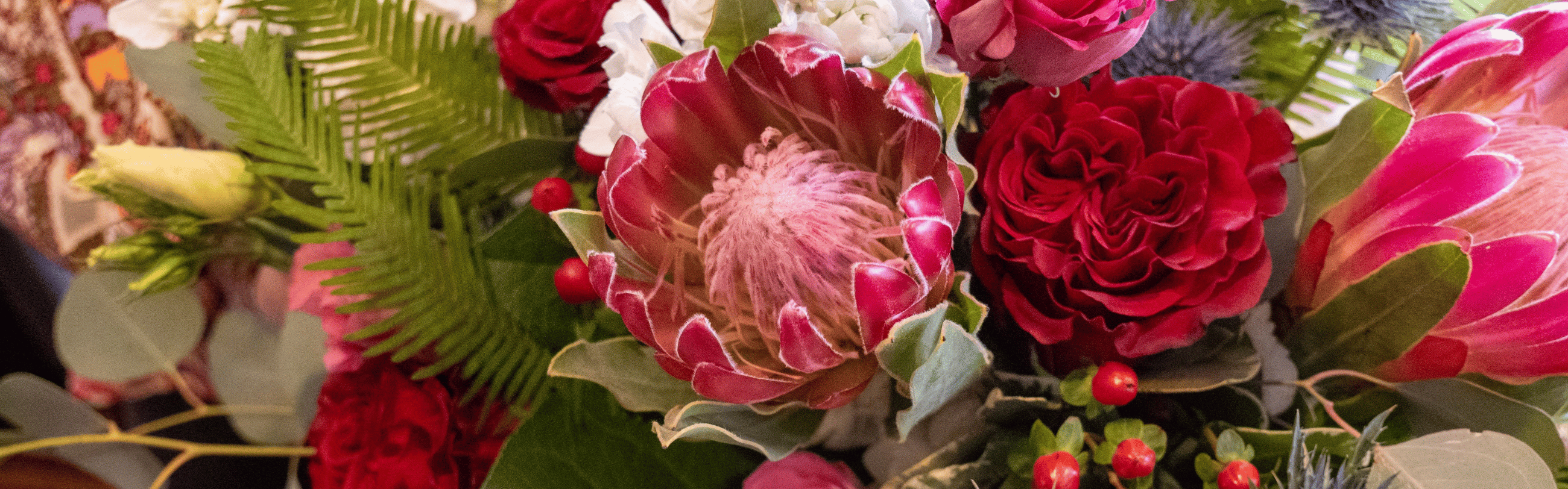 Pink King Protea, red roses, white flowers, and green foliage bouquet with red berries.